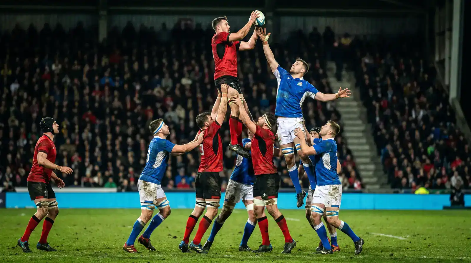 Premiership rugby match in progress with players competing at a line-out under stadium floodlights