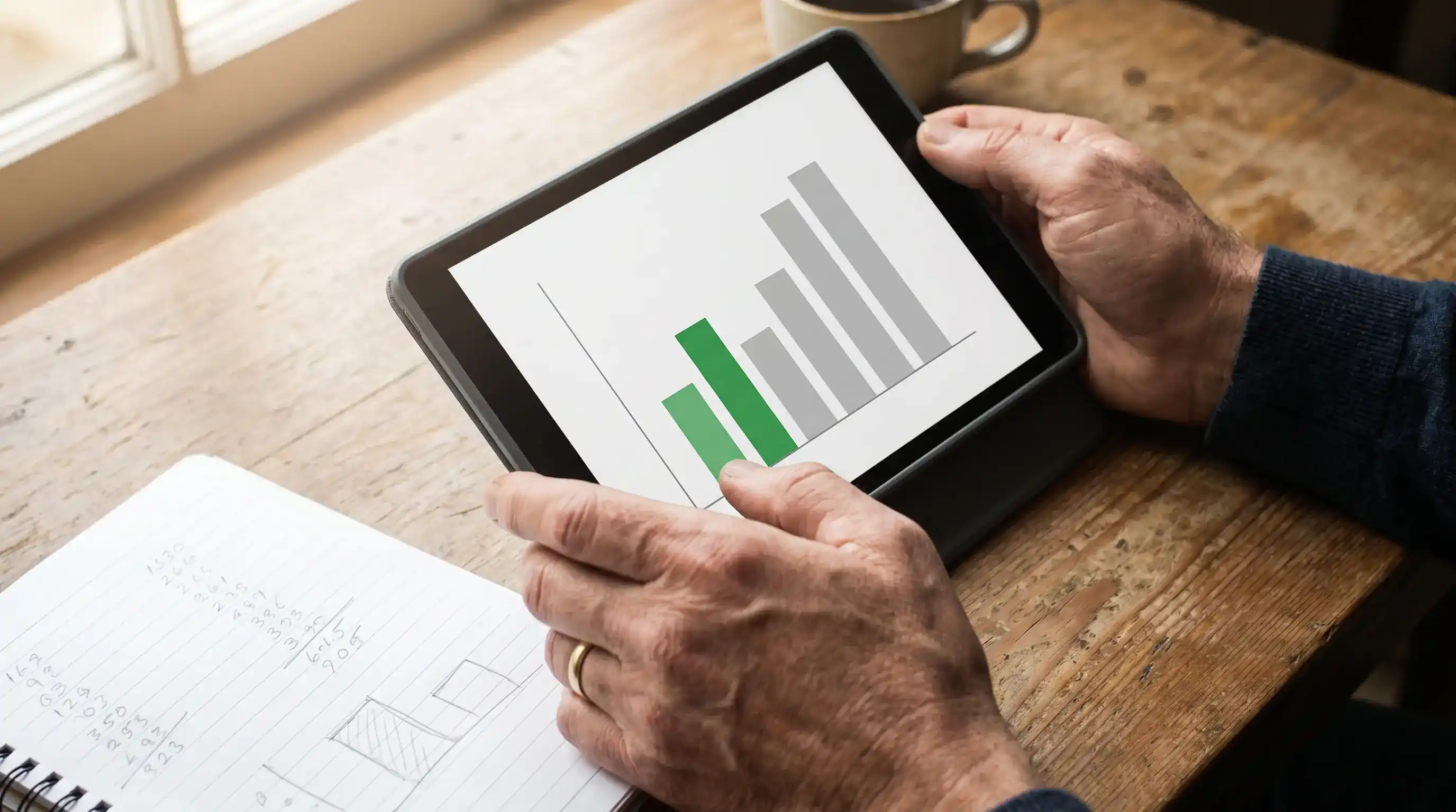 Close-up of a person reviewing rugby match statistics on a tablet with a notepad alongside