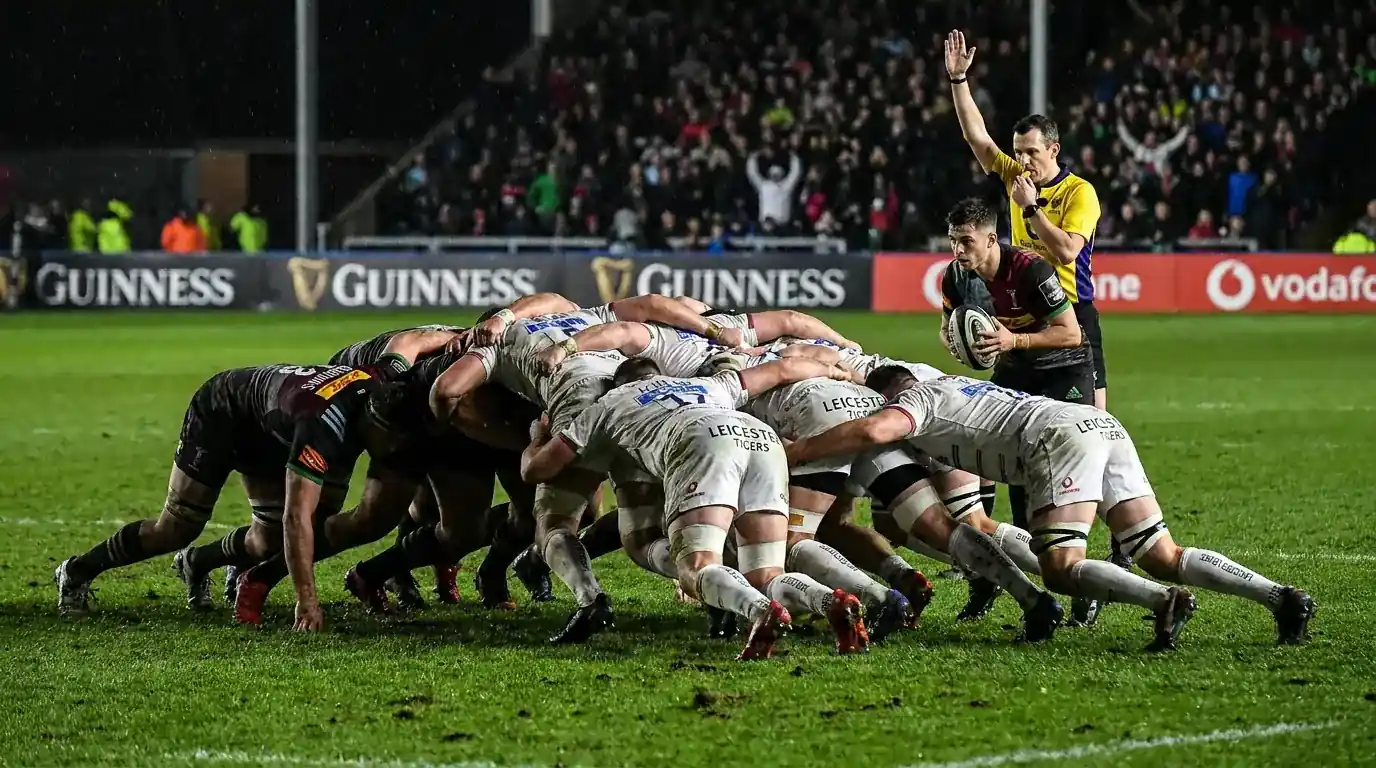 Rugby union forwards locked in a scrum during a Premiership match with referee watching closely